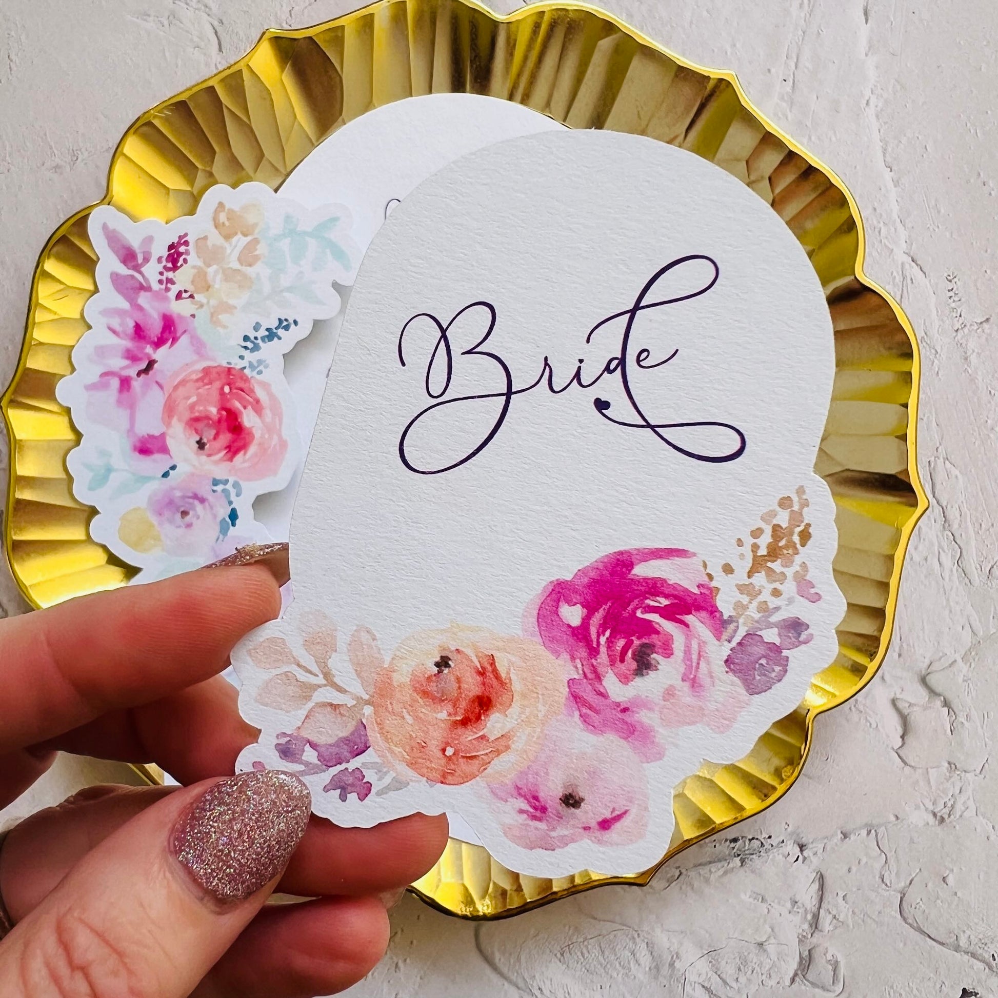 Wedding die cut Place Card with 'Bride' text and floral designs on a gold plate.