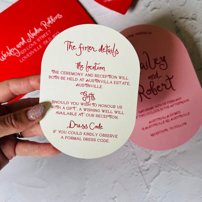 Oval wedding invitation card with red text held by a hand on a light background