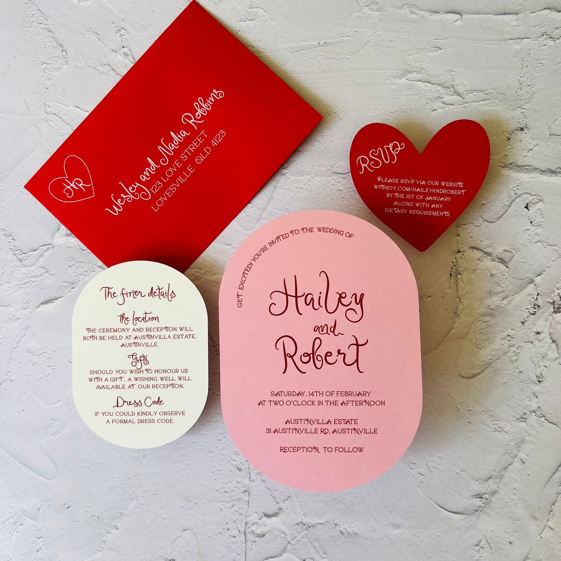 Set of wedding invitations with red, pink, and white cards on a textured surface.