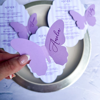 Butterfly-shaped purple wedding name cards with cursive text on a round silver tray.