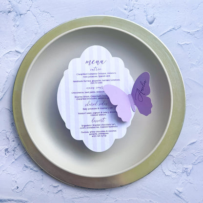 Round gold plate with a white card featuring a purple butterfly design on a light gray background