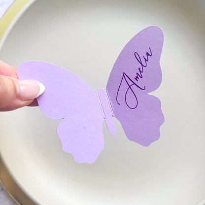 Purple butterfly-shaped card with 'Amelia' written on it, held by a hand against a white background.