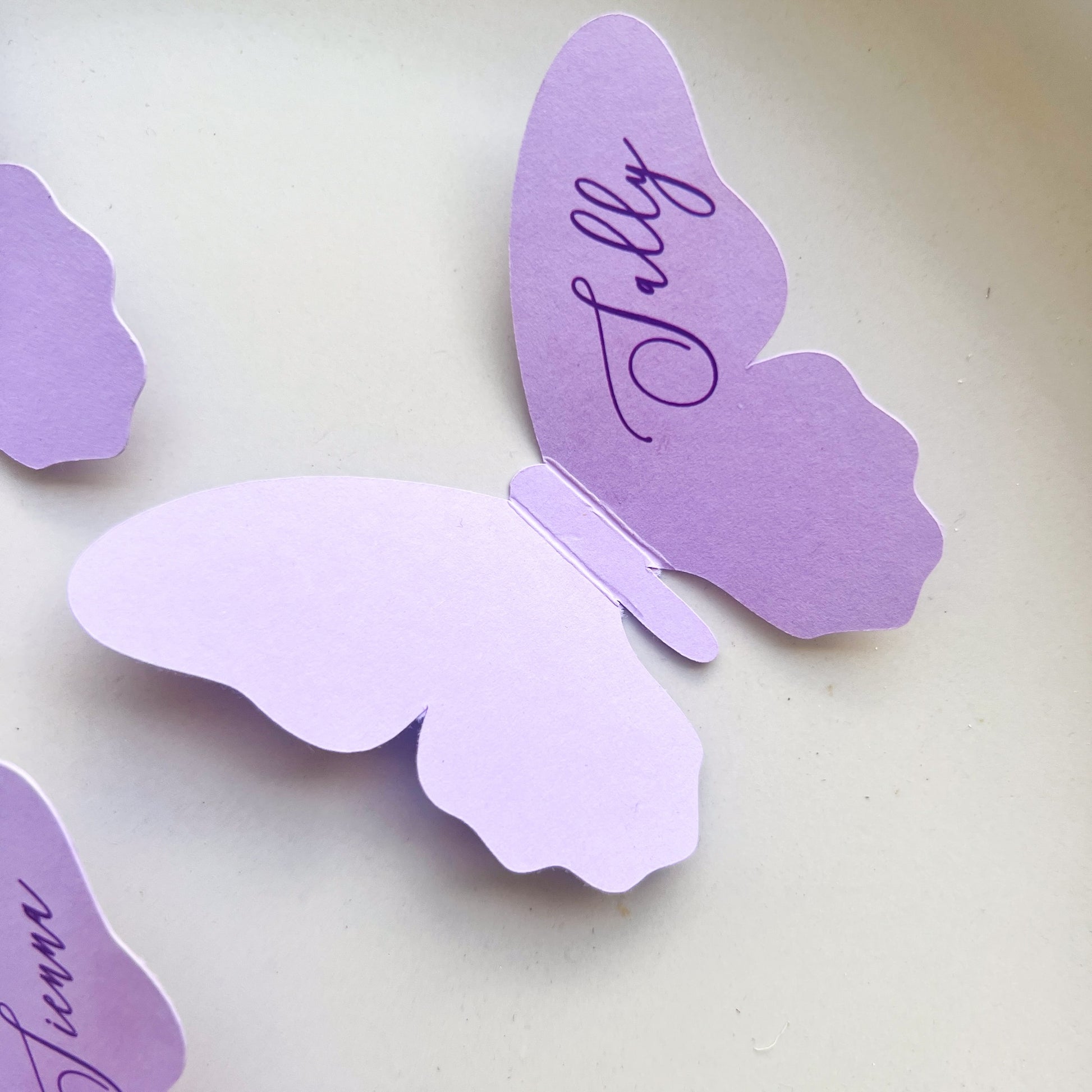 Butterfly-shaped purple wedding place cards with names on a light background