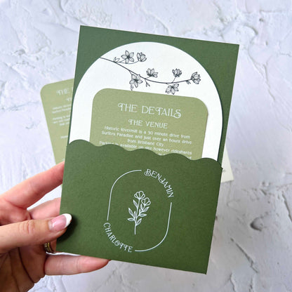 Green invitation card with floral design held by a hand on a light gray background