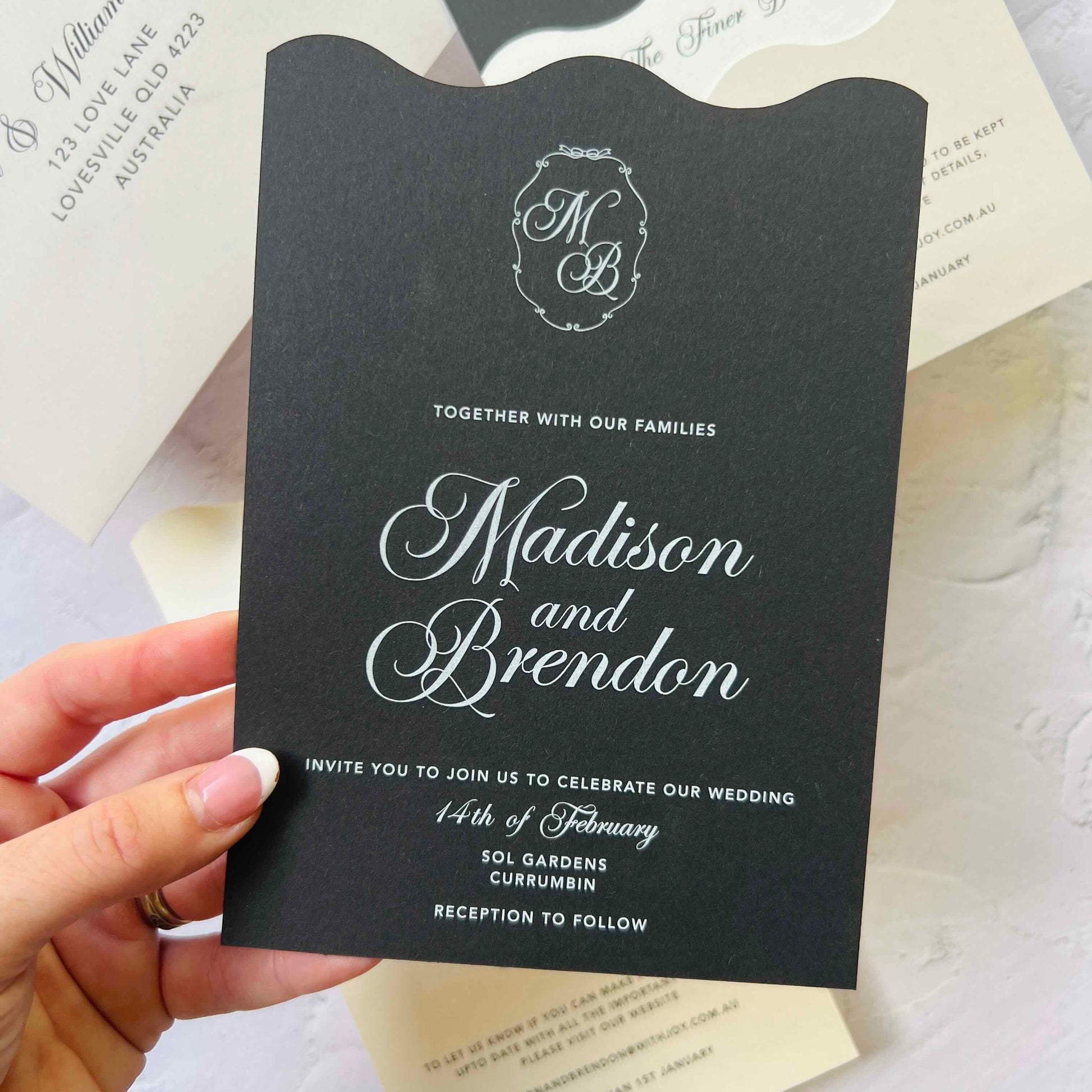 Black wedding invitation with white text held by a hand