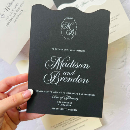 Black wedding invitation with white text held by a hand