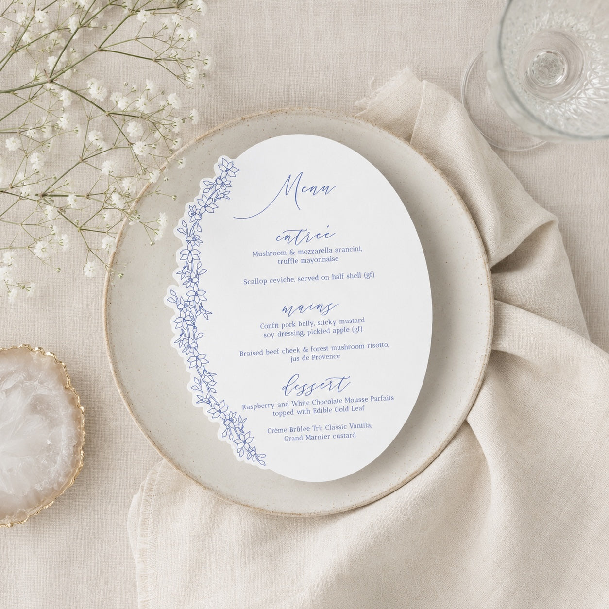 Menu card on a ceramic plate with floral design, placed on a beige napkin with baby's breath flowers.