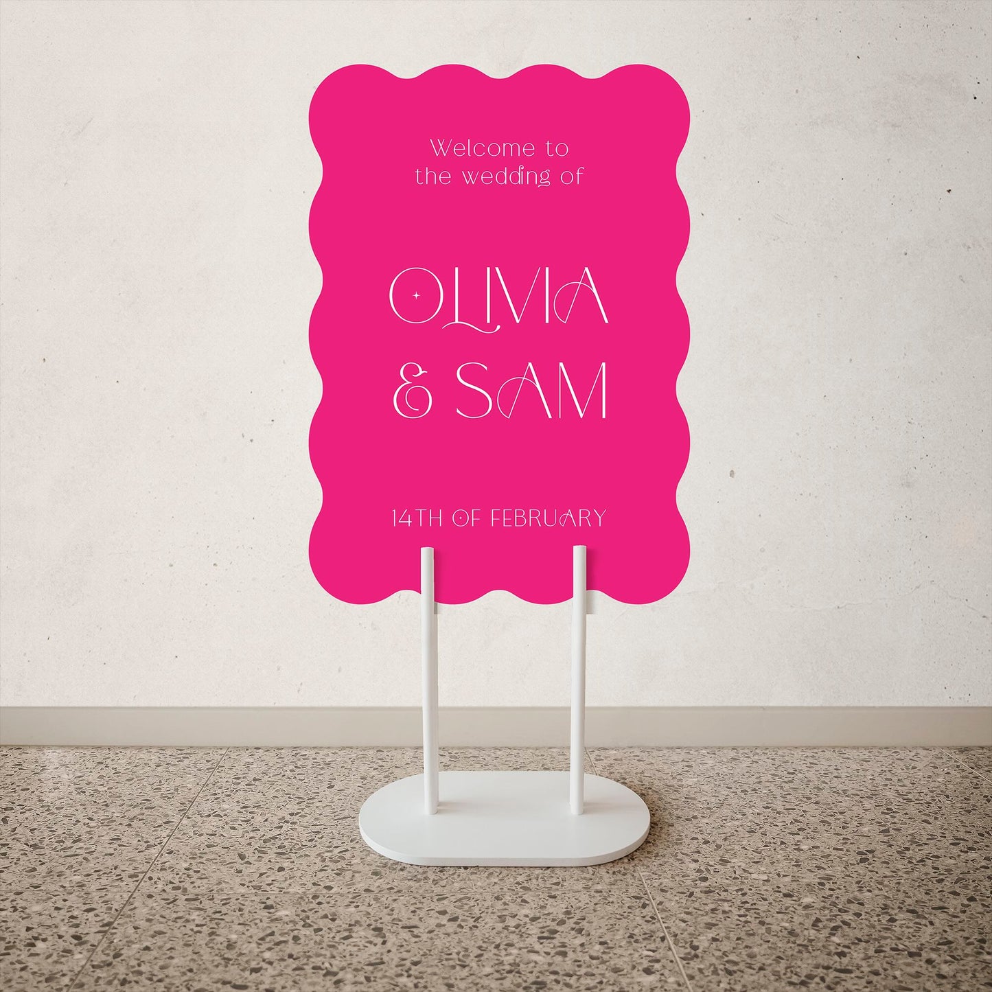 Wave Shape Wedding Welcome Sign Pink wedding sign with white text on a stand against a light gray wall.
