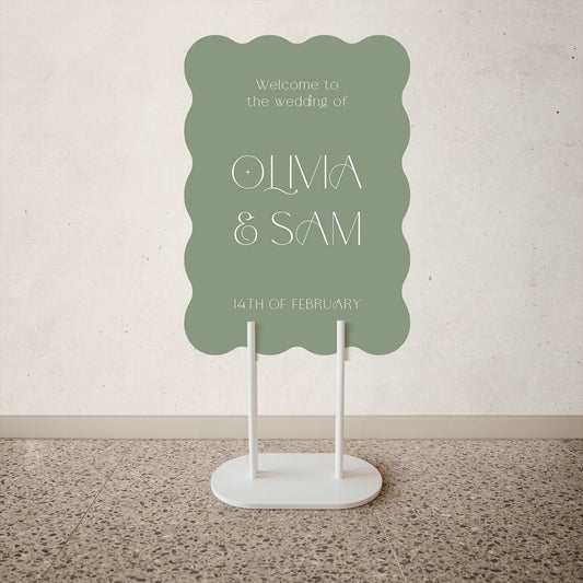 Sage Green Wedding welcome sign with 'Olivia & Sam' on a stand against a plain wall.