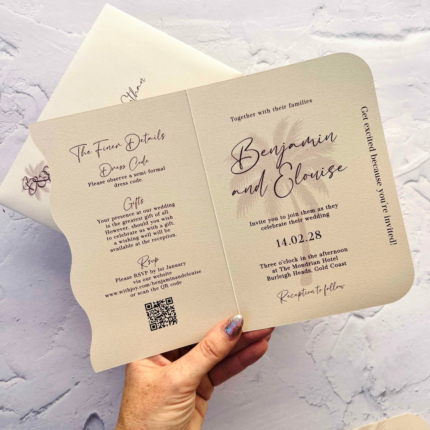 Wedding invitation card held by a hand with a QR code on a textured surface