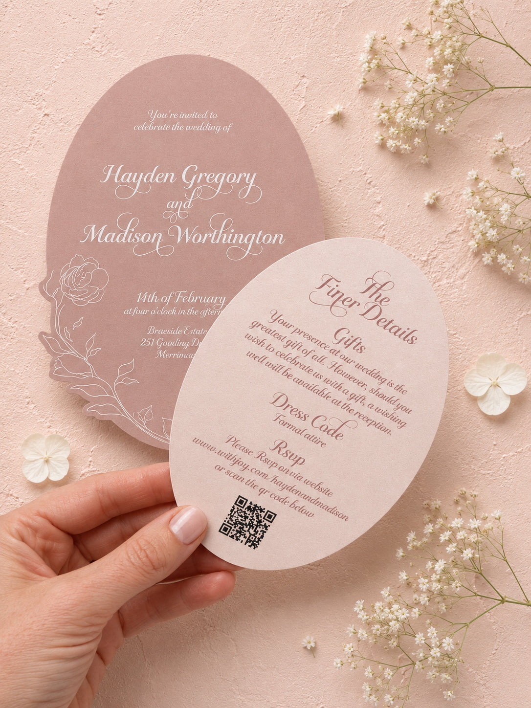 Wedding invitation card with QR code held by a hand on a pink background with flowers.